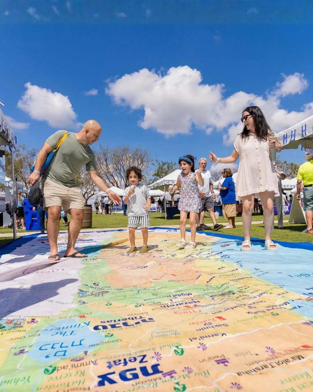 A family walks hand in hand across a giant map of Israel at an outdoor community festival